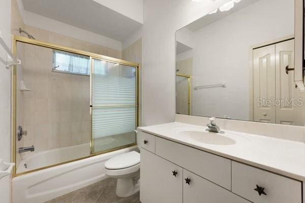 full bathroom with bath / shower combo with glass door, tile patterned flooring, vanity, and toilet