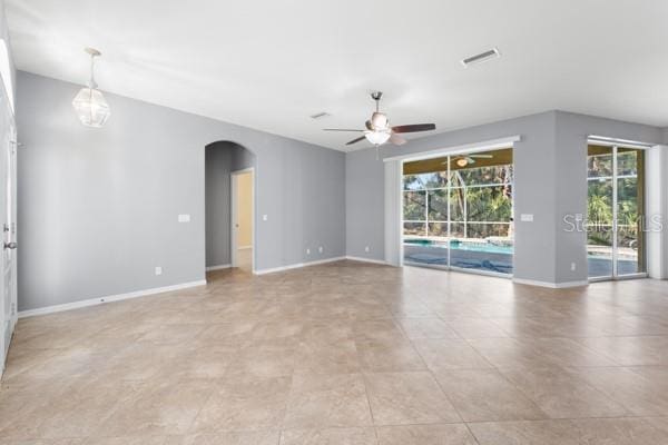 unfurnished room featuring baseboards, visible vents, arched walkways, and a ceiling fan