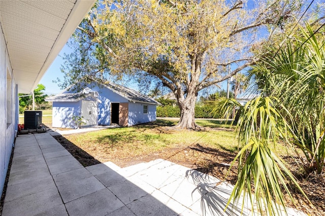 view of yard featuring central air condition unit, a patio area, and an outbuilding