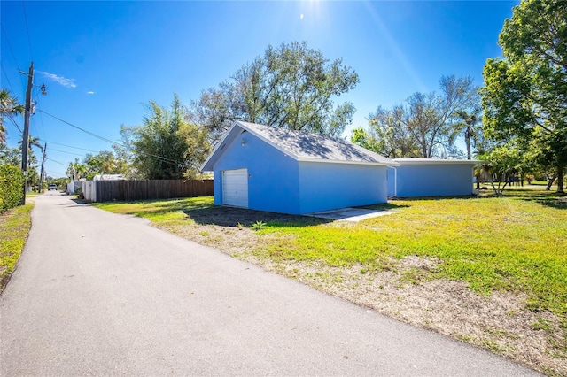 exterior space featuring a garage, driveway, a lawn, fence, and stucco siding