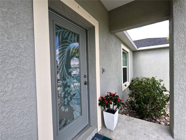 view of exterior entry with roof with shingles and stucco siding
