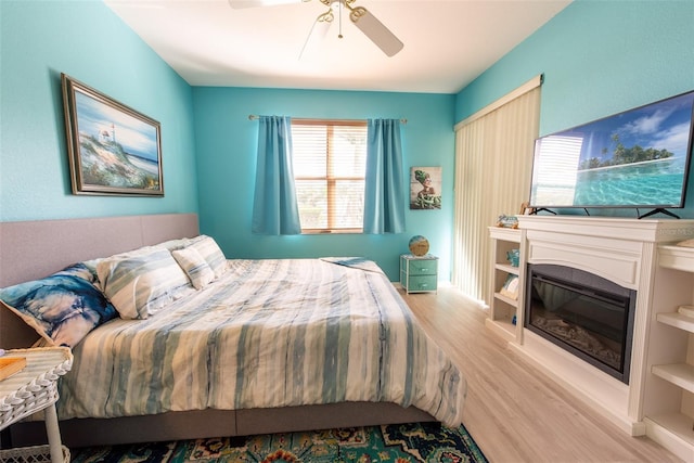 bedroom with a glass covered fireplace, ceiling fan, and wood finished floors