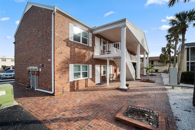 back of property with stairs, brick siding, a patio area, and a balcony