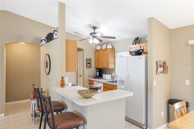 kitchen featuring light tile patterned floors, a breakfast bar, a peninsula, ceiling fan, and white fridge with ice dispenser