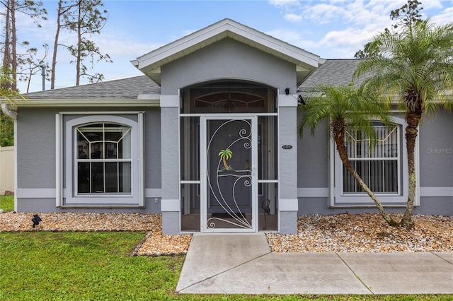 view of exterior entry featuring stucco siding and roof with shingles