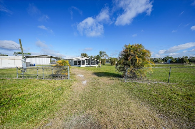 view of yard with a detached carport, a fenced backyard, and a sunroom
