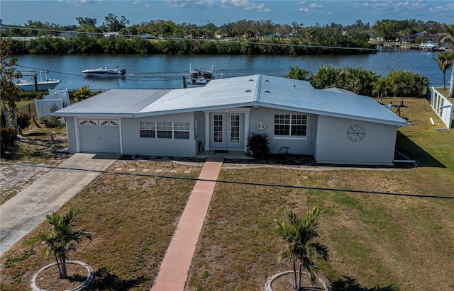 ranch-style house with an attached garage, a water view, fence, french doors, and a front yard