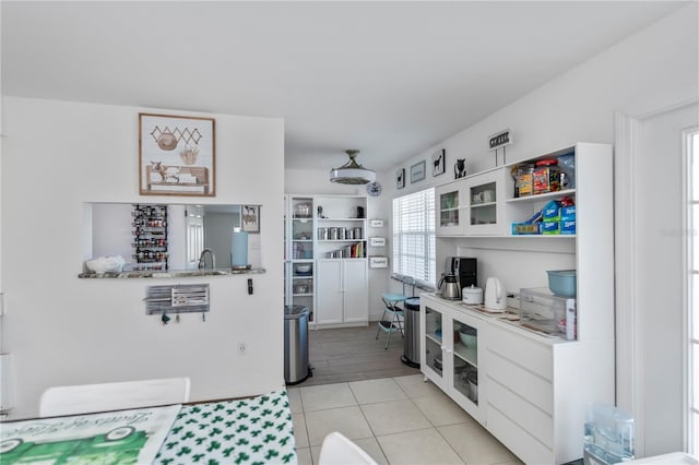 kitchen featuring light tile patterned floors, white cabinets, light countertops, open shelves, and glass insert cabinets