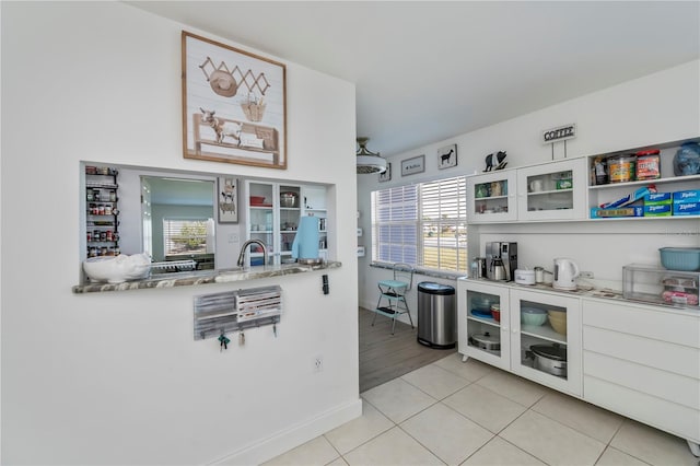 kitchen with glass insert cabinets, white cabinets, a healthy amount of sunlight, and light tile patterned floors