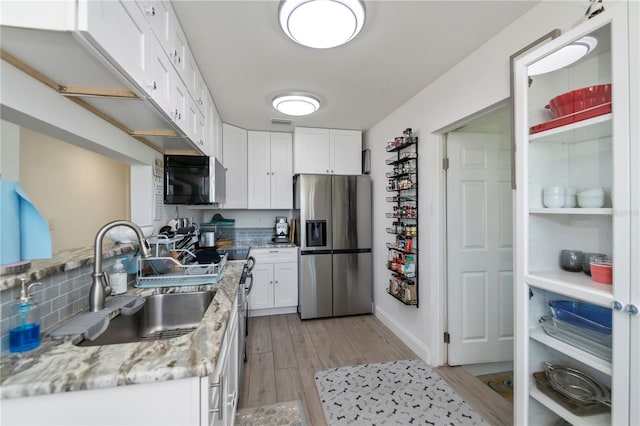 kitchen with a sink, white cabinetry, appliances with stainless steel finishes, light wood-type flooring, and light stone countertops