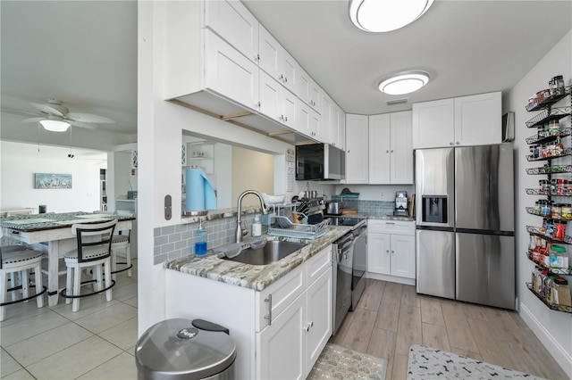 kitchen featuring light stone counters, stainless steel appliances, decorative backsplash, white cabinetry, and a sink