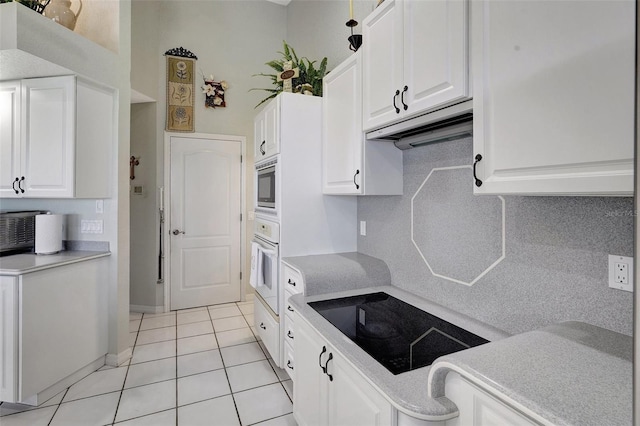 kitchen with oven, black electric stovetop, light countertops, under cabinet range hood, and white cabinetry