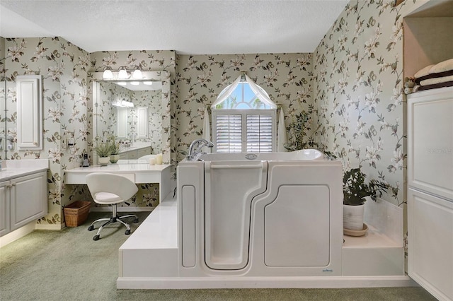 full bath with a bath, vanity, a textured ceiling, and wallpapered walls