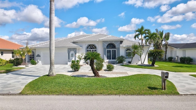 mediterranean / spanish-style house featuring a garage, concrete driveway, a tiled roof, stucco siding, and a front lawn