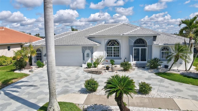 mediterranean / spanish house featuring driveway, stucco siding, an attached garage, and a tiled roof