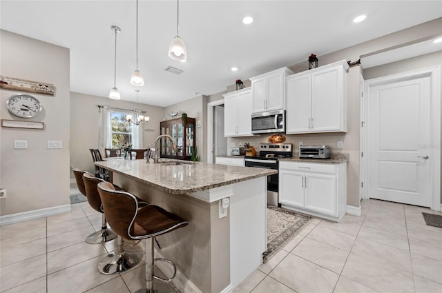 kitchen featuring pendant lighting, stainless steel appliances, white cabinetry, a sink, and an island with sink