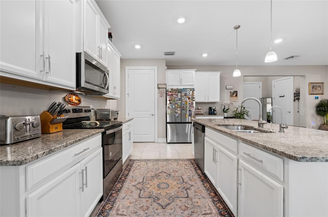 kitchen with decorative light fixtures, a sink, white cabinetry, appliances with stainless steel finishes, and a center island with sink