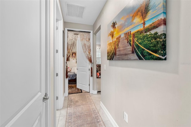 corridor featuring baseboards, visible vents, and light tile patterned flooring