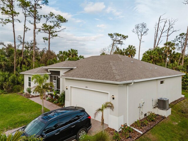 view of front of house featuring roof with shingles, stucco siding, an attached garage, cooling unit, and a front lawn