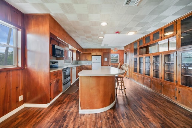 kitchen featuring visible vents, brown cabinetry, stainless steel appliances, light countertops, and wood walls