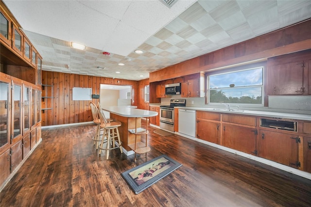 kitchen featuring dark wood-style floors, light countertops, appliances with stainless steel finishes, a sink, and a kitchen breakfast bar