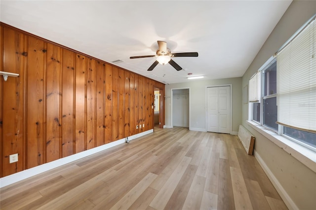 unfurnished bedroom with light wood-type flooring, a ceiling fan, baseboards, and two closets