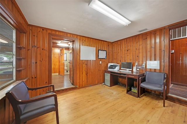 office featuring light wood finished floors, wooden walls, visible vents, and ornamental molding