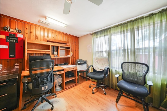 office featuring light wood-type flooring, wood walls, ceiling fan, and visible vents