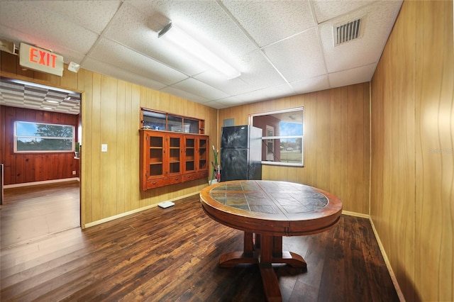 dining area with a paneled ceiling, visible vents, wooden walls, and hardwood / wood-style floors