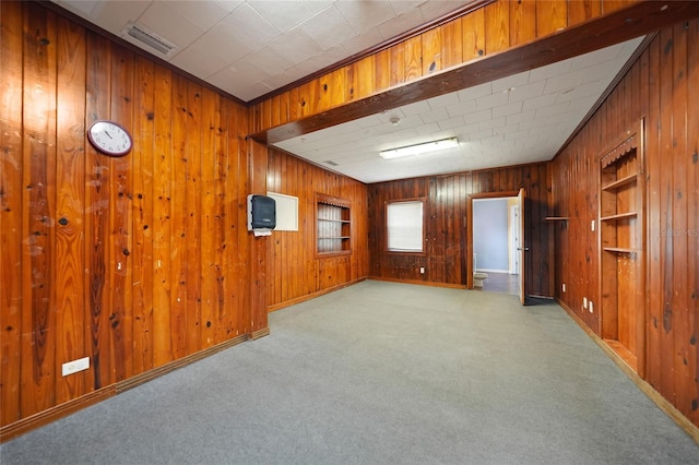 unfurnished room featuring carpet floors, built in shelves, visible vents, wood walls, and baseboards