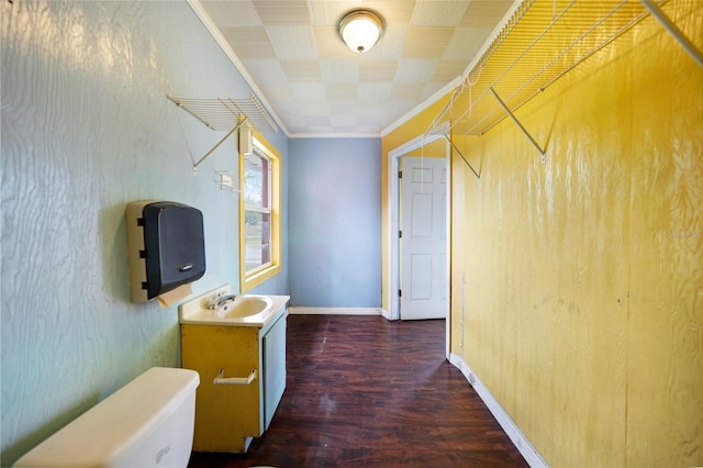 hall featuring ornamental molding, a sink, baseboards, and dark wood-style floors