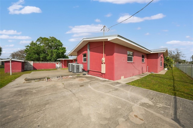 view of property exterior featuring an outbuilding, central AC, fence, a lawn, and stucco siding