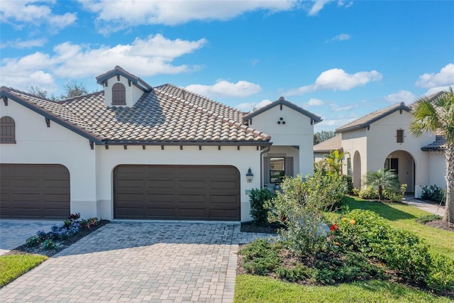 mediterranean / spanish-style home with stucco siding, an attached garage, a tile roof, and decorative driveway