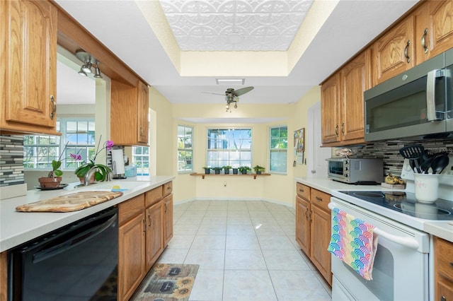 kitchen with white electric range oven, a tray ceiling, a toaster, black dishwasher, and stainless steel microwave