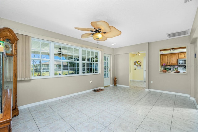 empty room with light tile patterned floors, a ceiling fan, visible vents, and baseboards