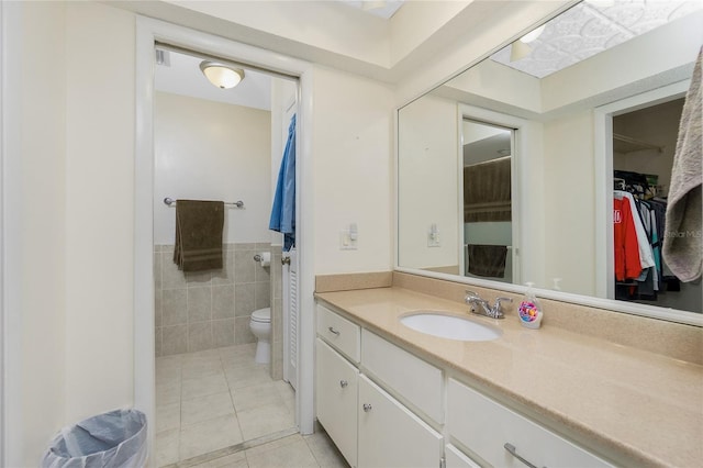 full bath with vanity, tile patterned flooring, a walk in closet, tile walls, and toilet