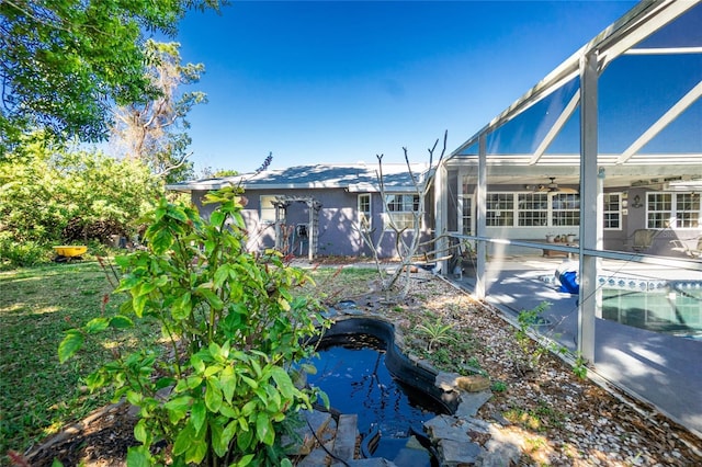 view of yard with ceiling fan, an outdoor pool, glass enclosure, and a patio