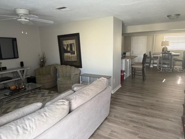 living area with a textured ceiling, a ceiling fan, visible vents, and light wood-style floors