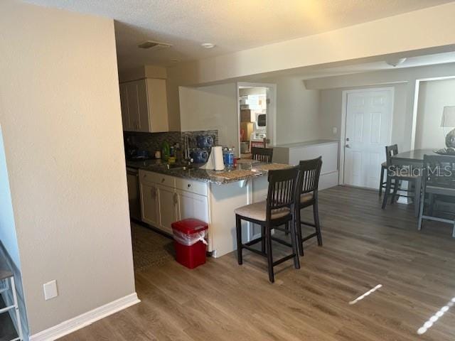 kitchen with a kitchen bar, backsplash, a sink, wood finished floors, and baseboards