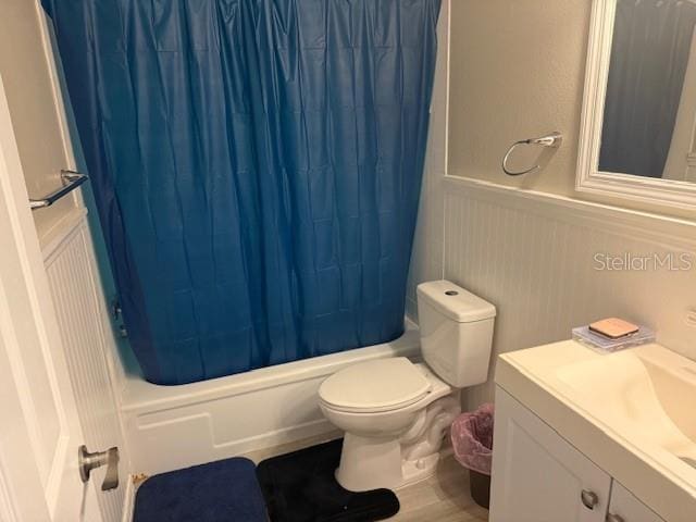 bathroom with toilet, wainscoting, vanity, and shower / bathtub combination with curtain