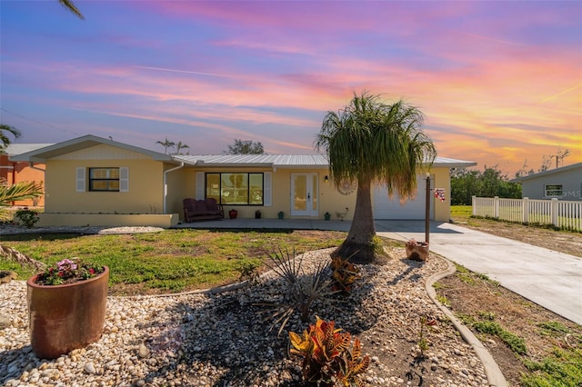 ranch-style house with driveway, metal roof, an attached garage, fence, and stucco siding