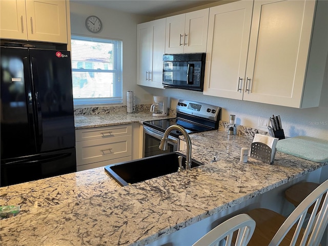 kitchen with light stone counters, white cabinetry, a sink, and black appliances