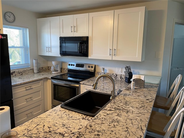 kitchen featuring light stone countertops, black appliances, white cabinets, and a sink