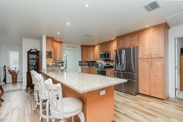 kitchen featuring visible vents, appliances with stainless steel finishes, a peninsula, a sink, and backsplash