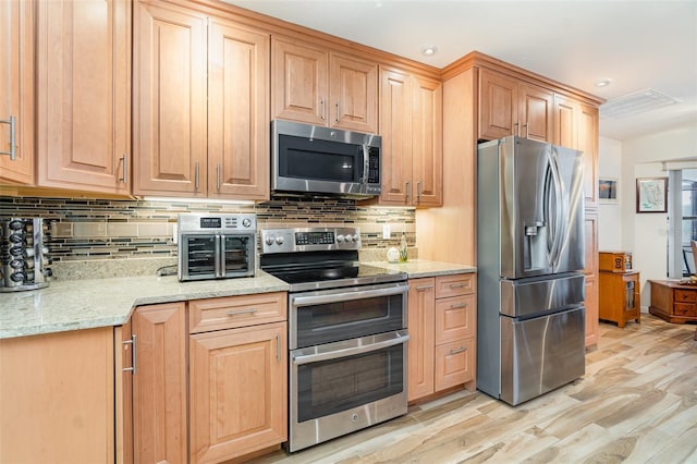 kitchen featuring light wood finished floors, stainless steel appliances, tasteful backsplash, and light stone counters