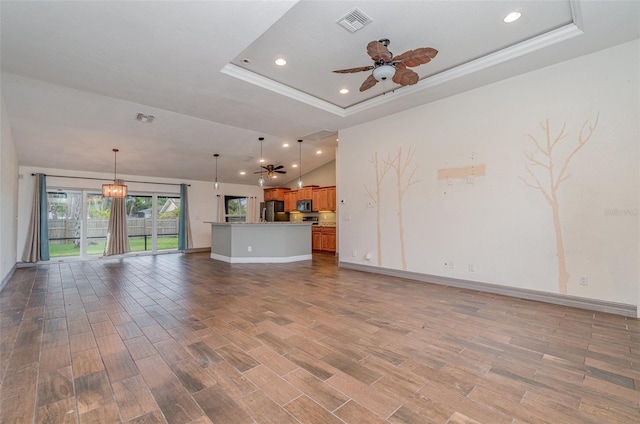 unfurnished living room featuring visible vents, ceiling fan, wood finished floors, a tray ceiling, and crown molding