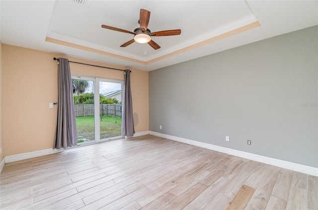 empty room with a tray ceiling, light wood-style flooring, a ceiling fan, ornamental molding, and baseboards