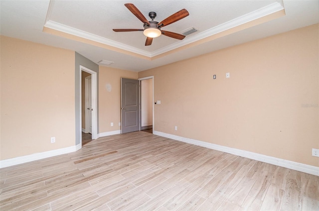 empty room with light wood finished floors, a tray ceiling, ornamental molding, and visible vents