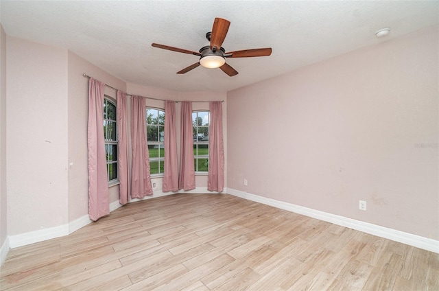 empty room featuring light wood finished floors, baseboards, and a textured ceiling