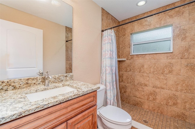 bathroom featuring toilet, tiled shower, and vanity